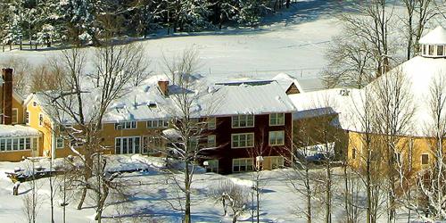 Large yellow house with barn covered in snow with barren trees in the foreground.