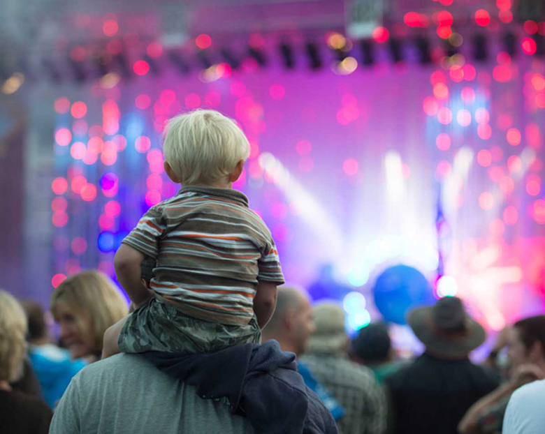 A young boy sits on his fathers' shoulders and watches up-and-coming artists at Grand Point North '15.
