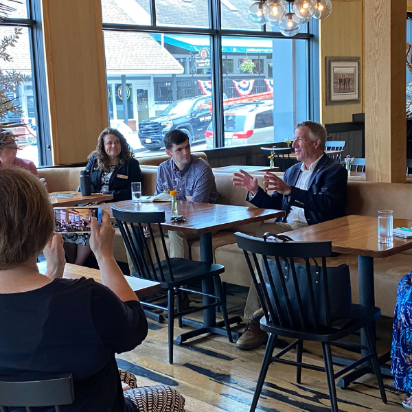 Several people seated at a restaurant for a group discussion. Governor Phil Scott is at the center speaking with raised hands. 