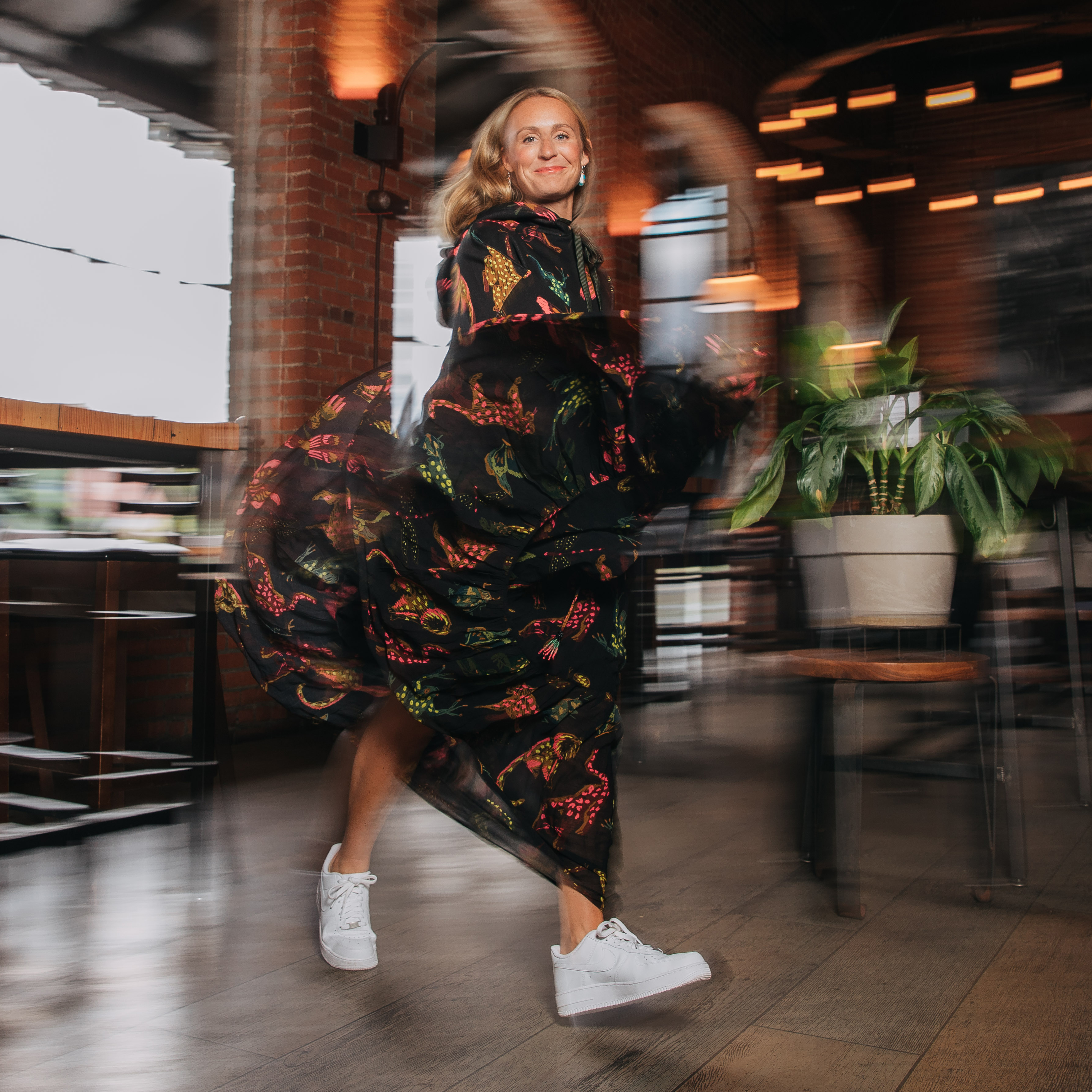 Person in a flowing, patterned dress twirling joyfully in a dimly-lit restaurant with exposed brick walls.