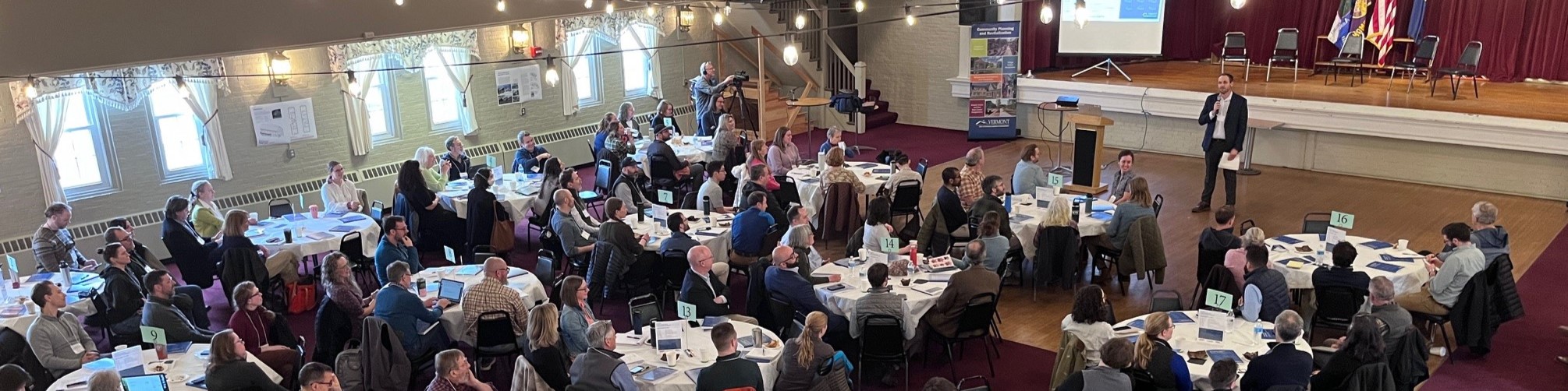 Large conference meeting - many small circular tables - presenter upfront