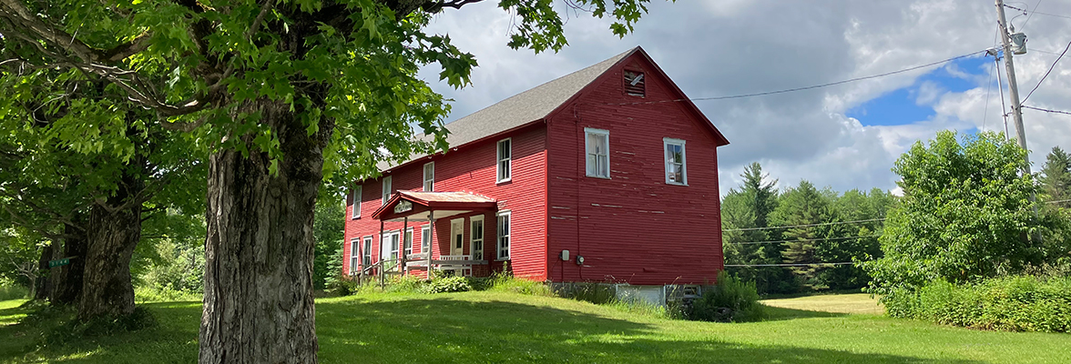 Red grange building with green field and oak trees