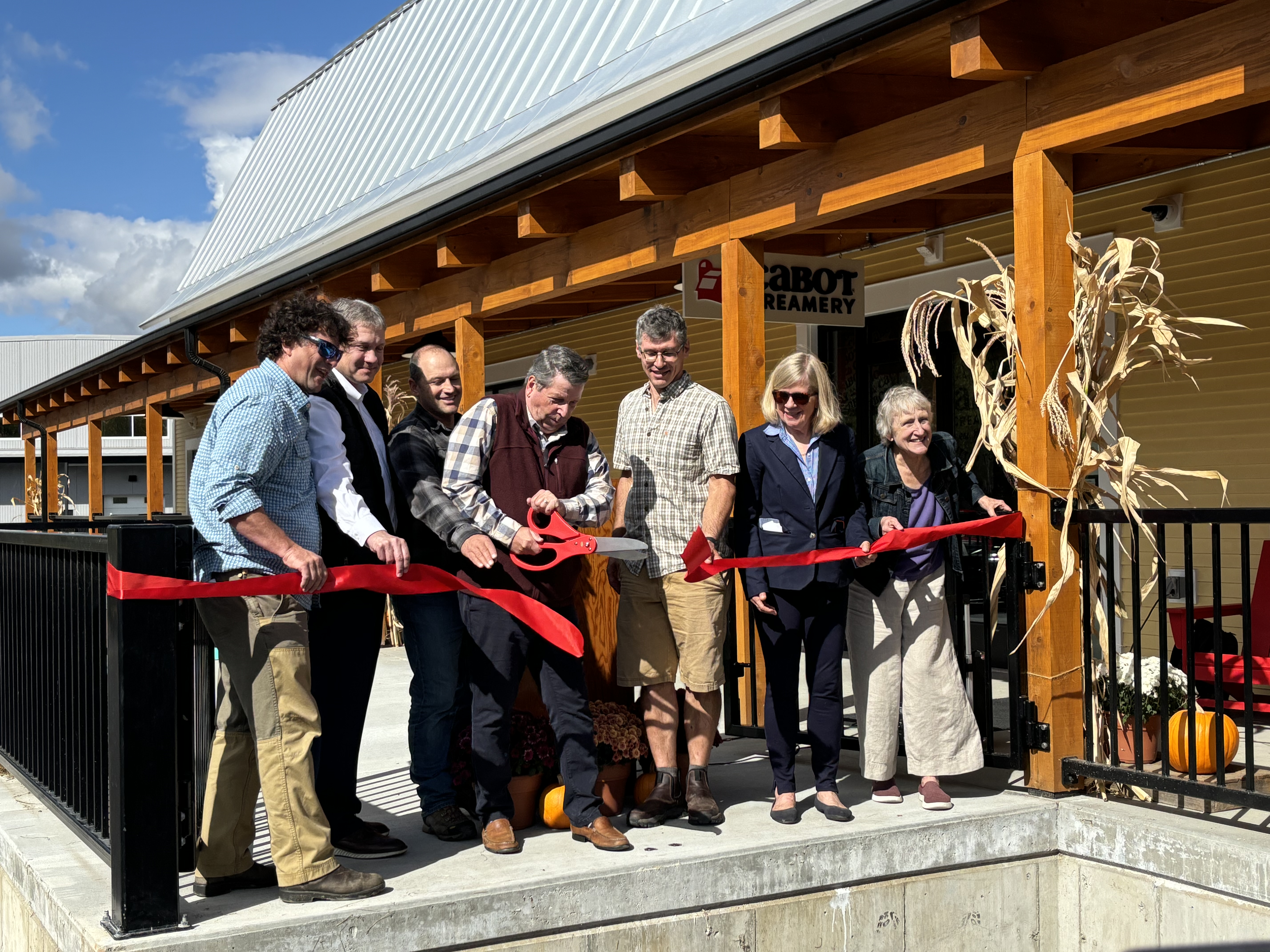 Group of people cutting ceremonial red ribbon. Man in the center is holding large scissors.