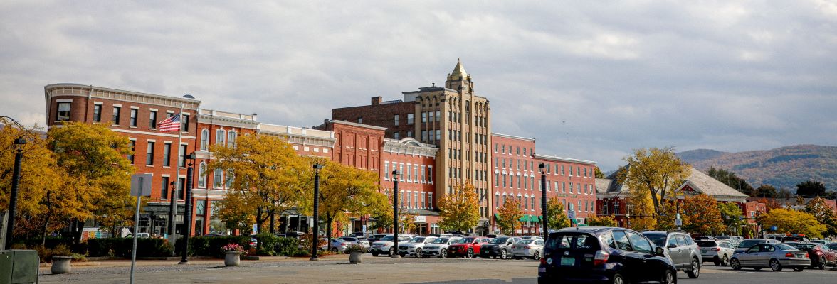 Downtown Rutland Vermont - Brick buildings line a busy street, it is fall and their is a tinge of orange to the mountain in the background of the photo