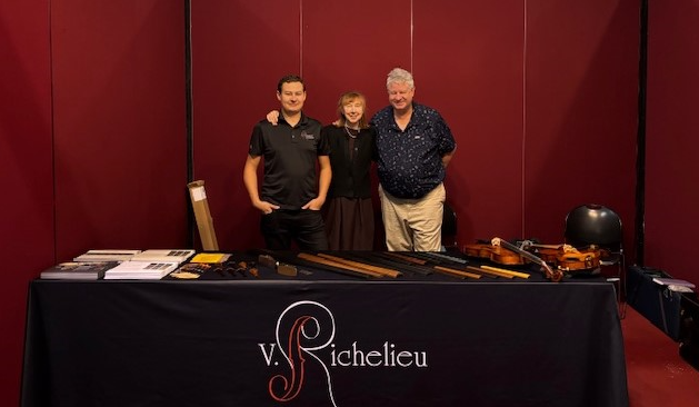 Three people standing in front of a large wall and behind a table with violin parts on it.